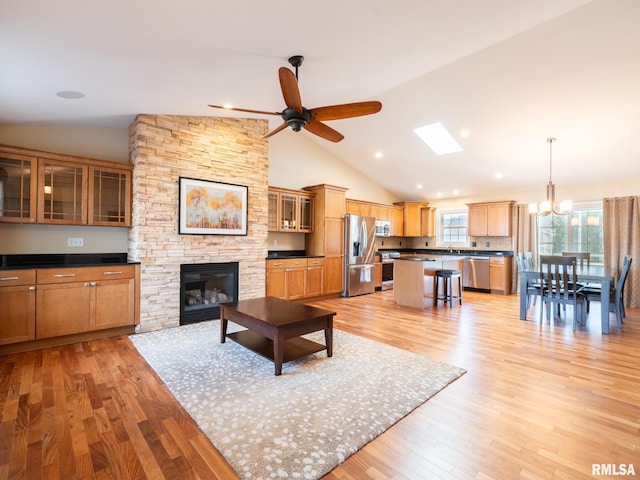 unfurnished living room featuring light wood-type flooring, ceiling fan with notable chandelier, a sink, recessed lighting, and a fireplace