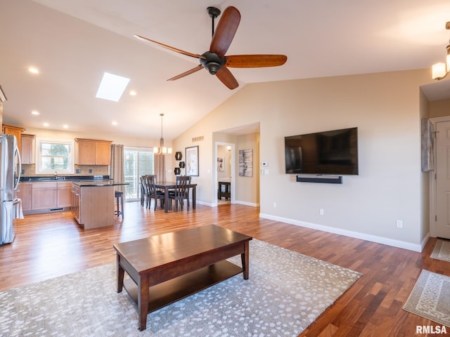 living area featuring a ceiling fan, baseboards, vaulted ceiling with skylight, recessed lighting, and light wood-style floors