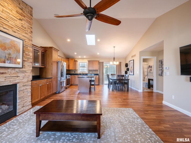 unfurnished living room with ceiling fan with notable chandelier, wood finished floors, a fireplace, and baseboards