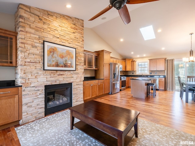 living area with ceiling fan with notable chandelier, recessed lighting, a stone fireplace, light wood finished floors, and vaulted ceiling