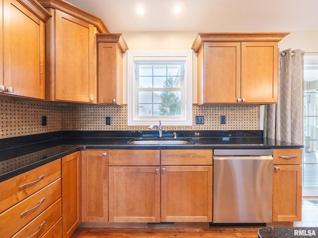 kitchen featuring tasteful backsplash, dishwasher, dark stone countertops, wood finished floors, and a sink