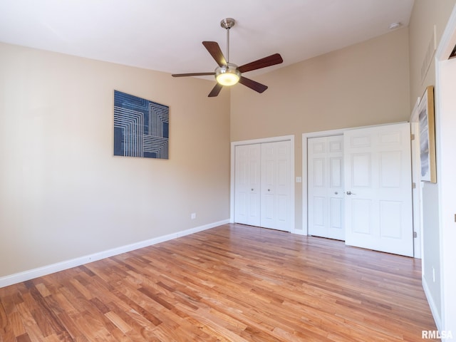 unfurnished bedroom featuring light wood-style floors, baseboards, two closets, and high vaulted ceiling