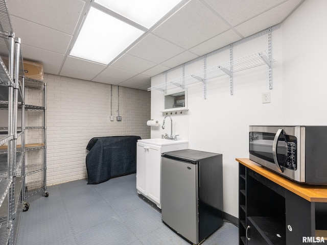 clothes washing area with tile patterned floors, brick wall, and a sink