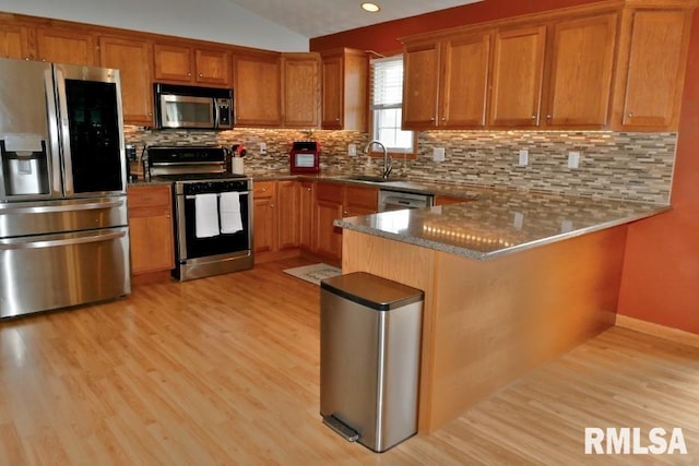 kitchen featuring light wood finished floors, decorative backsplash, brown cabinetry, stainless steel appliances, and a sink