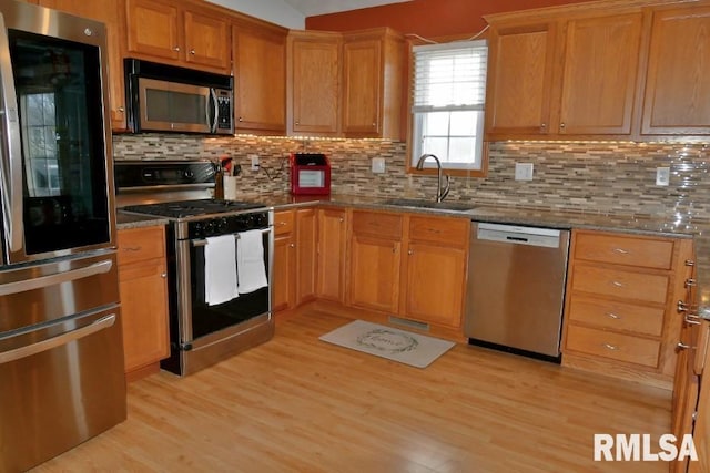 kitchen featuring a sink, light wood-style floors, stone counters, and stainless steel appliances