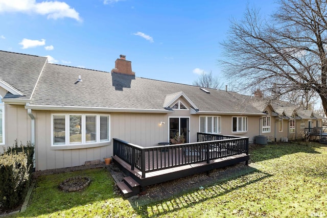 back of property featuring roof with shingles, a lawn, central AC, and a chimney