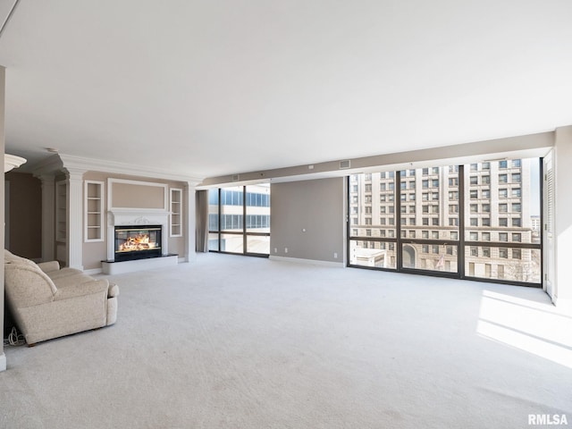 unfurnished living room featuring a glass covered fireplace, expansive windows, ornate columns, and carpet floors