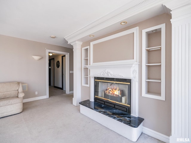 unfurnished living room featuring built in features, a glass covered fireplace, carpet flooring, baseboards, and ornate columns