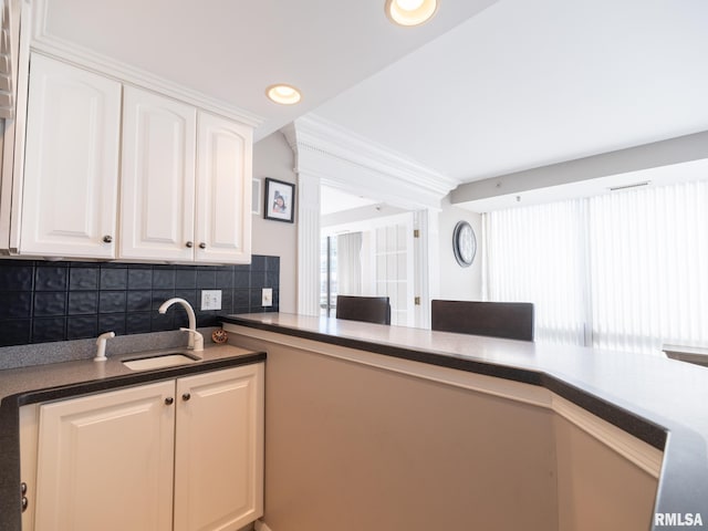 kitchen with dark countertops, decorative backsplash, recessed lighting, white cabinets, and a sink