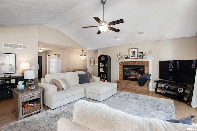 living area with visible vents, a brick fireplace, lofted ceiling, wood finished floors, and a ceiling fan