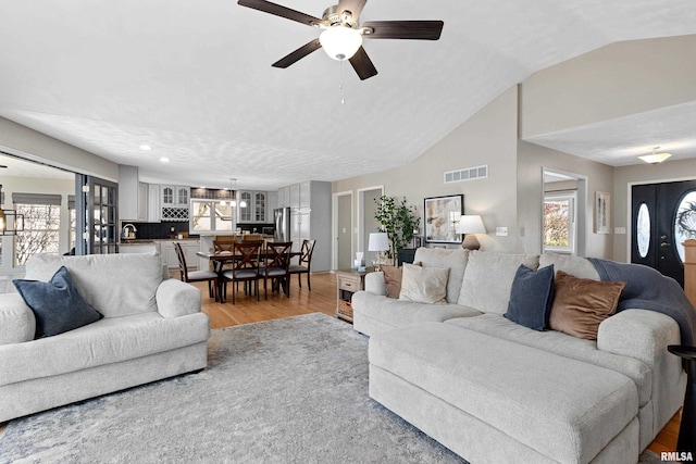 living room featuring visible vents, plenty of natural light, lofted ceiling, and light wood-style floors