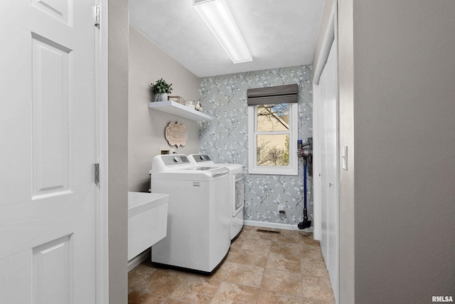 washroom featuring washing machine and clothes dryer, laundry area, wallpapered walls, and baseboards