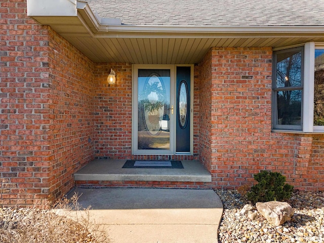 entrance to property with brick siding and a shingled roof