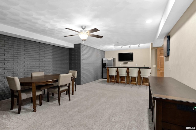 dining area featuring a ceiling fan, brick wall, rail lighting, a dry bar, and light colored carpet