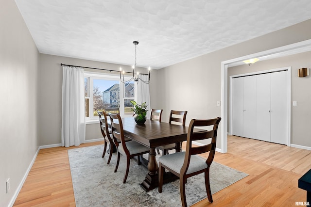 dining space with a notable chandelier, baseboards, and light wood-type flooring