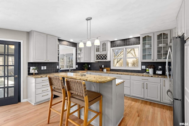 kitchen featuring backsplash, a kitchen island, glass insert cabinets, light wood-type flooring, and freestanding refrigerator