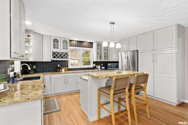 kitchen with light wood-style flooring, stainless steel refrigerator, a sink, backsplash, and white cabinets