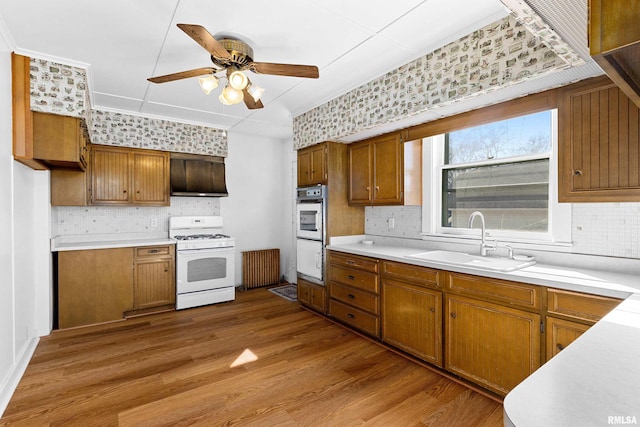 kitchen featuring a sink, white appliances, wood finished floors, and brown cabinetry