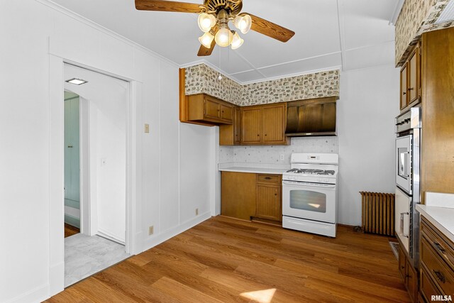 kitchen with brown cabinets, wood finished floors, white gas range oven, crown molding, and light countertops