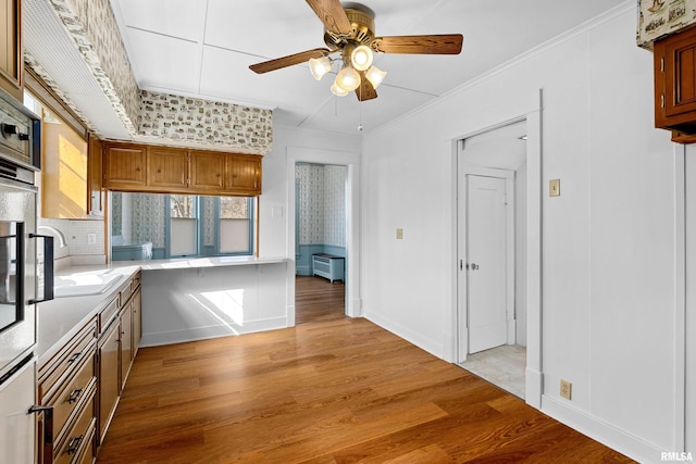 kitchen with ceiling fan, light countertops, ornamental molding, light wood-style flooring, and brown cabinetry