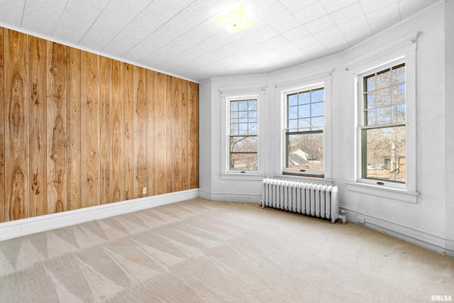 carpeted spare room with baseboards, radiator, and wooden walls