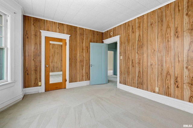 carpeted spare room with baseboards, wooden walls, and ornamental molding