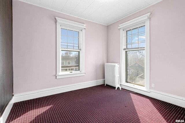 spare room featuring baseboards, radiator, and dark carpet