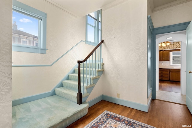 stairway featuring a textured wall, ornamental molding, baseboards, and wood-type flooring