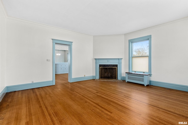 unfurnished living room featuring crown molding, wood finished floors, a fireplace, and radiator heating unit