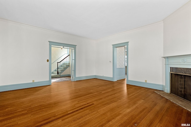 unfurnished living room with wood finished floors, baseboards, a high end fireplace, stairs, and crown molding