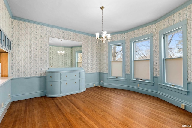 unfurnished dining area featuring wallpapered walls, wood finished floors, a wainscoted wall, and a chandelier