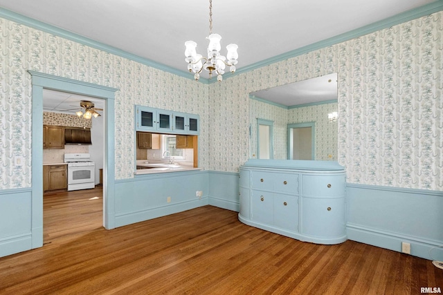 unfurnished dining area with wallpapered walls, ornamental molding, wood finished floors, and wainscoting