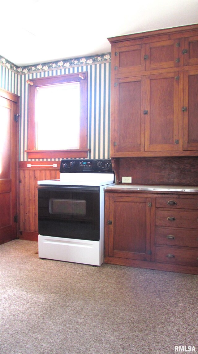 kitchen with light colored carpet, wallpapered walls, electric stove, and brown cabinets