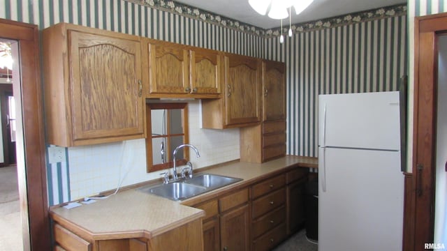 kitchen featuring wallpapered walls, light countertops, freestanding refrigerator, and a sink