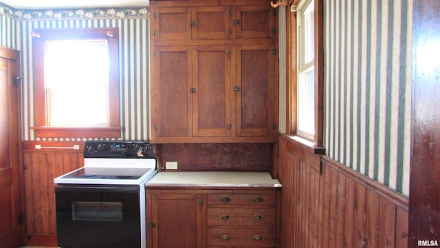 kitchen featuring a wealth of natural light, a wainscoted wall, brown cabinets, and range with electric stovetop