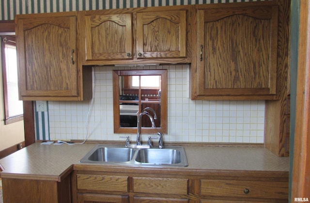 kitchen with a sink, tasteful backsplash, brown cabinetry, and light countertops