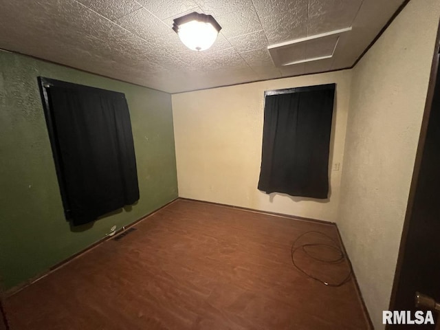 empty room with wood finished floors, a textured wall, and a textured ceiling