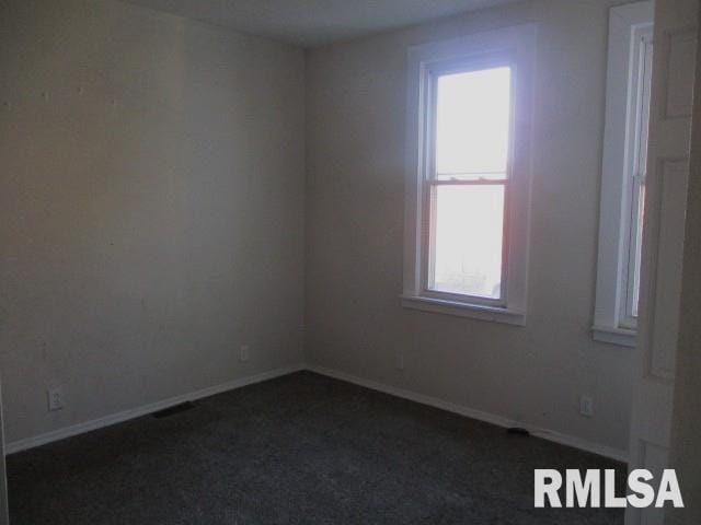 spare room featuring baseboards and dark carpet