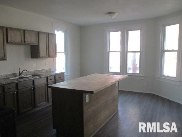 kitchen featuring a sink, a kitchen island, light countertops, baseboards, and dark wood-style flooring