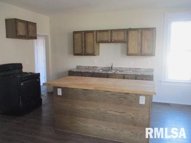 kitchen featuring wooden counters, dark wood-style flooring, a sink, black range with gas stovetop, and a center island