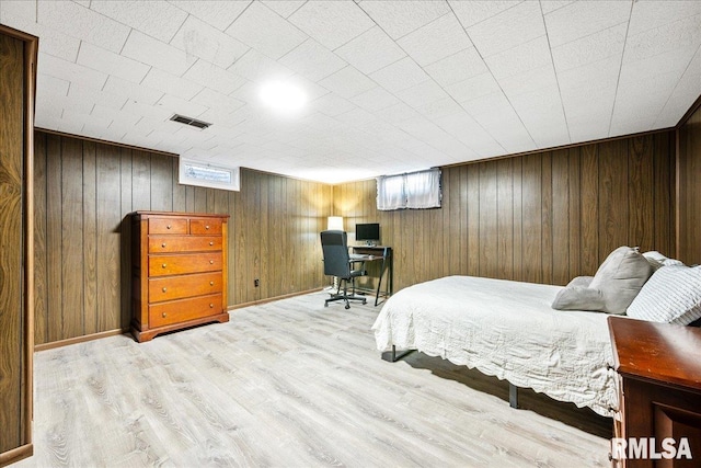 bedroom featuring wooden walls, visible vents, baseboards, and wood finished floors