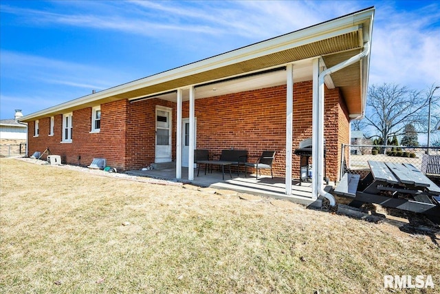 rear view of house featuring a patio, a yard, fence, and brick siding