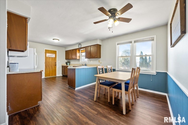 dining area featuring dark wood-type flooring, a ceiling fan, a wainscoted wall, and baseboards