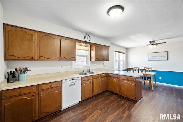 kitchen featuring dishwasher, light countertops, a peninsula, dark wood-style floors, and a sink