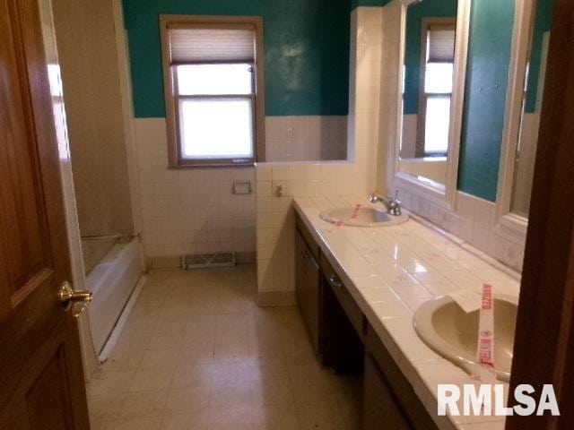 full bathroom featuring double vanity, a tub, tile walls, and a sink