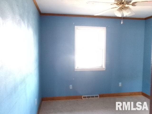 empty room featuring crown molding, carpet flooring, baseboards, and visible vents