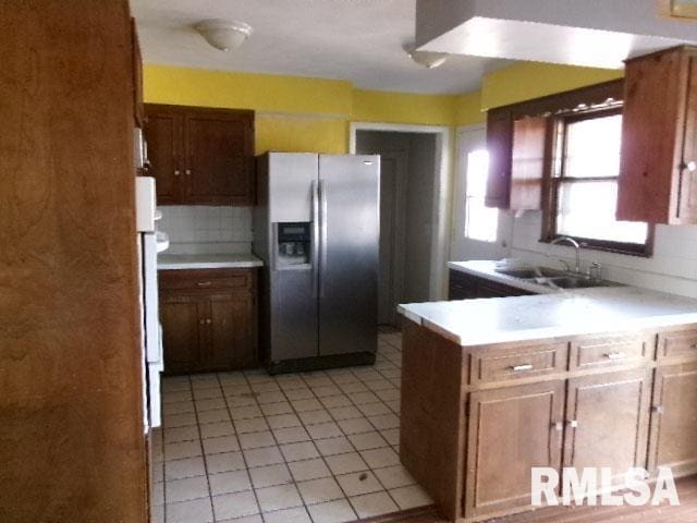 kitchen featuring a sink, backsplash, stainless steel fridge, a peninsula, and light countertops