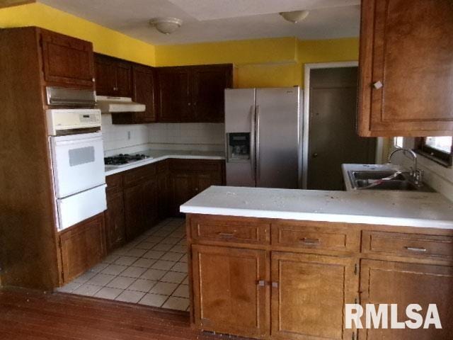 kitchen with gas stovetop, a sink, white oven, a warming drawer, and stainless steel fridge