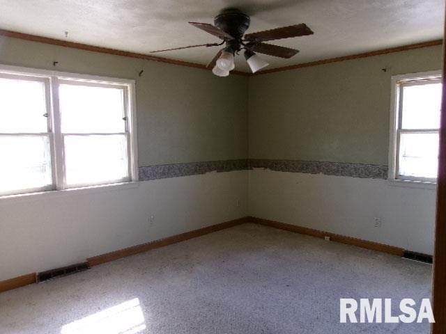 spare room with visible vents, a ceiling fan, baseboards, and ornamental molding