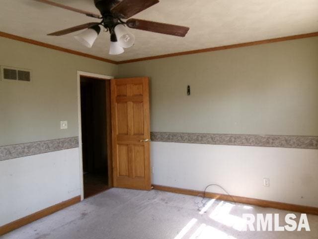 spare room featuring visible vents, crown molding, carpet, ceiling fan, and wainscoting